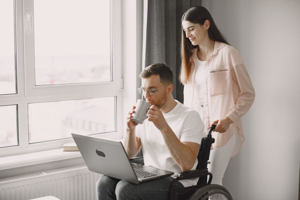 A support worker assisting a man with a warm drink while he works at home